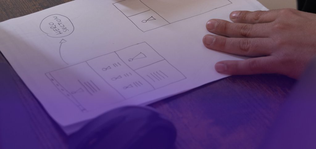 foglio con disegnato il wireframe di un sito web e una mano appoggiata sopra